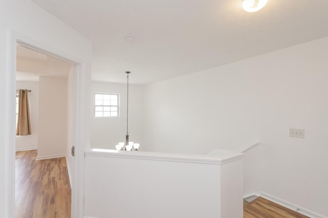 corridor featuring light wood-style floors, baseboards, a notable chandelier, and an upstairs landing