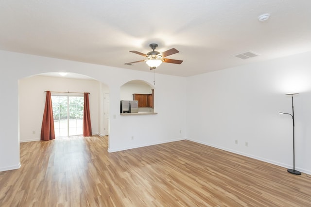 unfurnished living room featuring light wood-type flooring, baseboards, visible vents, and arched walkways