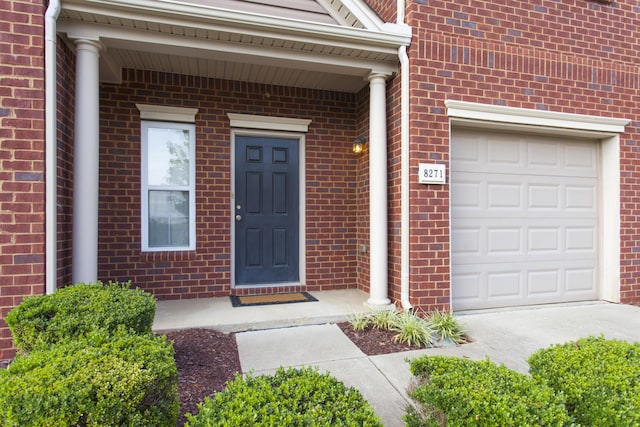 view of exterior entry with a garage and brick siding