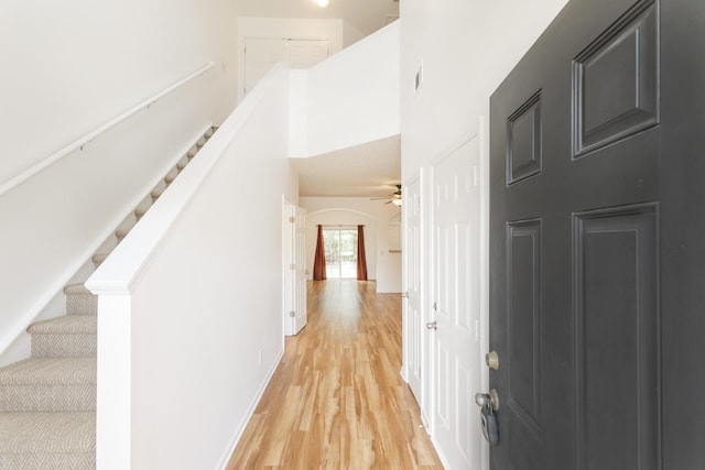 interior space featuring baseboards, arched walkways, a towering ceiling, stairs, and light wood-style floors