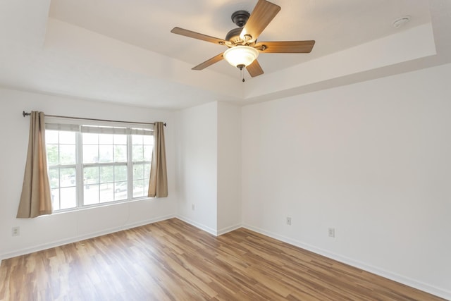 unfurnished room featuring a tray ceiling, ceiling fan, baseboards, and wood finished floors