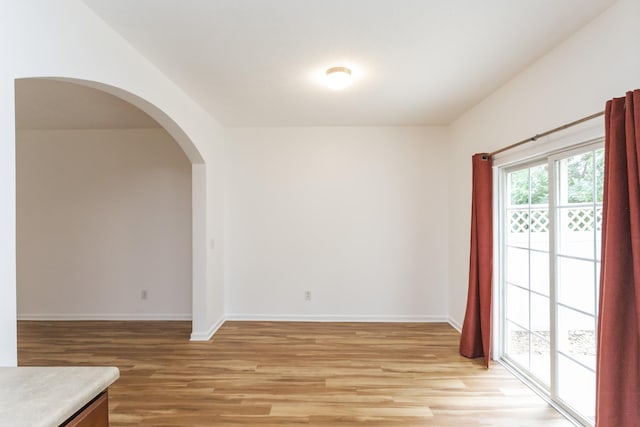 unfurnished room featuring light wood-style floors, arched walkways, and baseboards