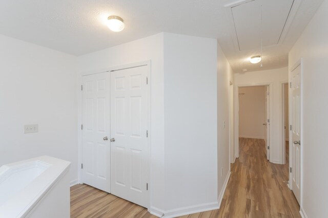 hall featuring light wood-style floors, attic access, and baseboards