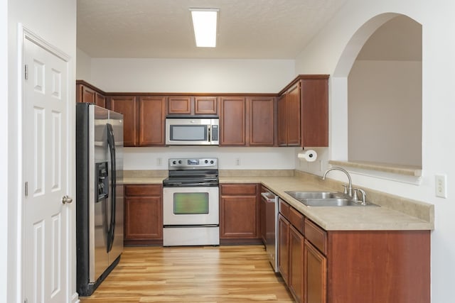 kitchen featuring stainless steel appliances, light countertops, light wood-style flooring, a sink, and a textured ceiling