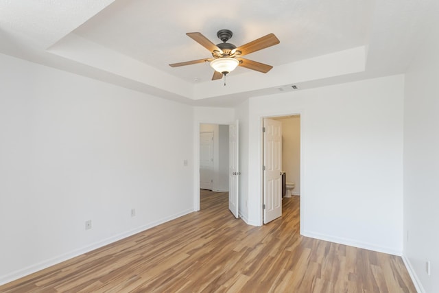 spare room featuring light wood-type flooring, visible vents, baseboards, and a raised ceiling