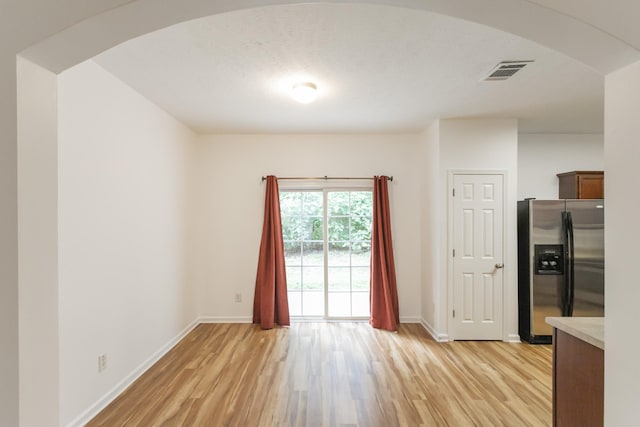 interior space with arched walkways, light wood-style flooring, visible vents, and baseboards