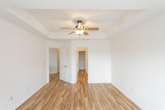 empty room featuring light wood finished floors, baseboards, a tray ceiling, and ceiling fan