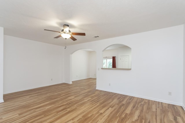 spare room featuring arched walkways, visible vents, baseboards, a ceiling fan, and light wood-type flooring