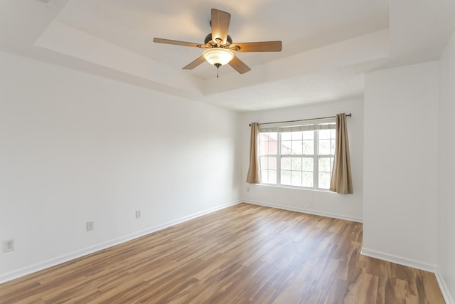 empty room featuring a ceiling fan, a tray ceiling, baseboards, and wood finished floors