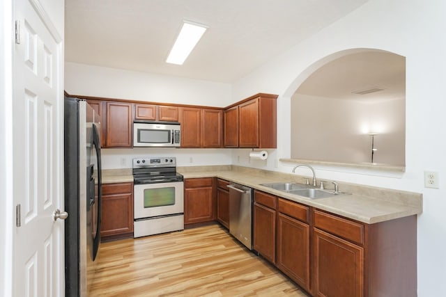 kitchen featuring light wood finished floors, appliances with stainless steel finishes, brown cabinets, light countertops, and a sink