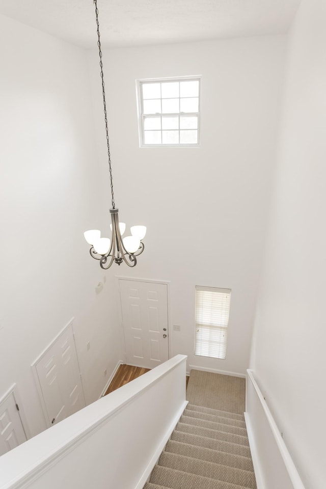 stairway with a notable chandelier, carpet floors, a towering ceiling, and baseboards