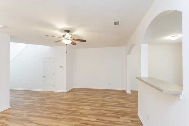 unfurnished room with arched walkways, visible vents, light wood-style floors, a ceiling fan, and baseboards