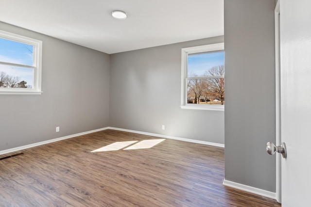 unfurnished room with visible vents, wood finished floors, a wealth of natural light, and baseboards