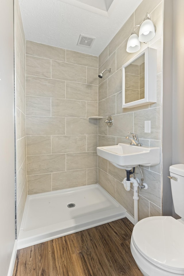 full bath with visible vents, toilet, a sink, wood finished floors, and tiled shower