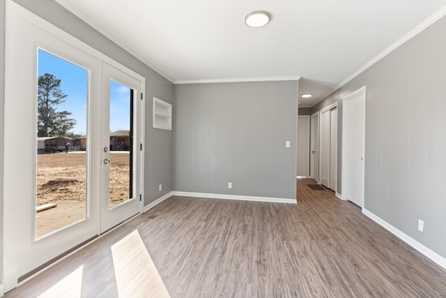 spare room featuring crown molding, baseboards, and wood finished floors