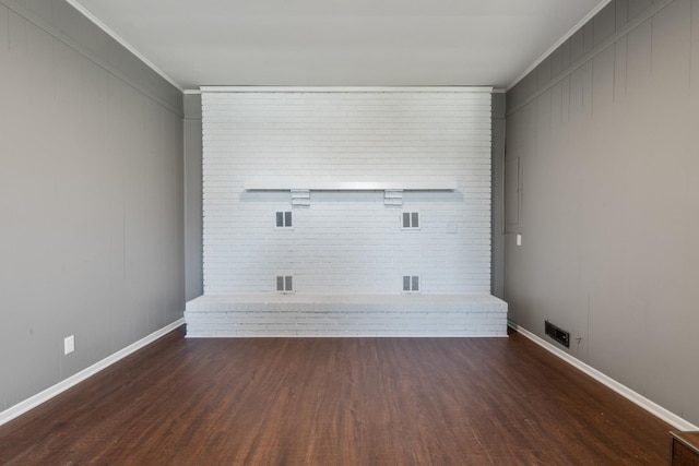 empty room featuring brick wall, baseboards, crown molding, and wood finished floors