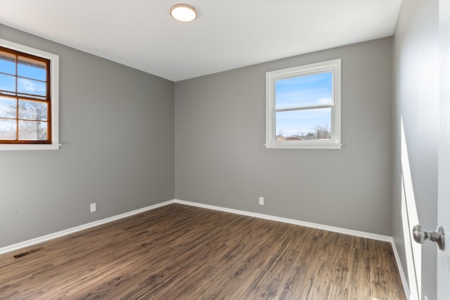 unfurnished room featuring dark wood-type flooring, visible vents, and baseboards