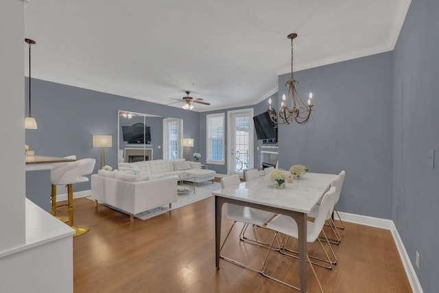 dining space featuring baseboards, ceiling fan, ornamental molding, wood finished floors, and a fireplace