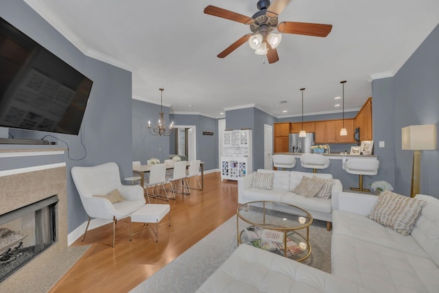 living area featuring a fireplace with flush hearth, crown molding, baseboards, and wood finished floors