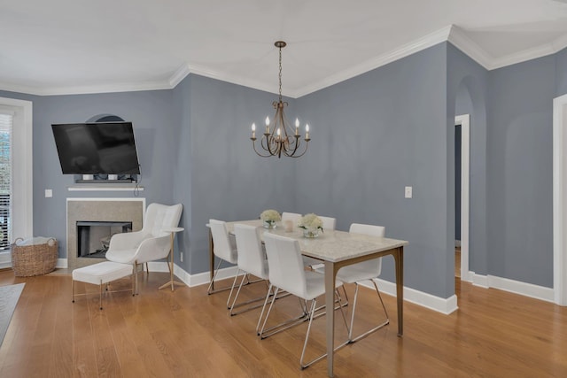 dining area featuring crown molding, a fireplace, baseboards, and light wood-style floors