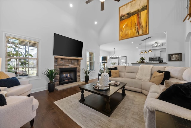 living room featuring baseboards, a ceiling fan, dark wood-style floors, a high ceiling, and a fireplace