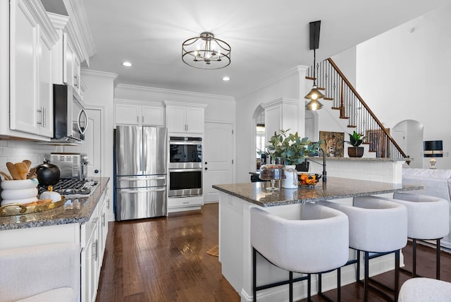 kitchen featuring white cabinets, arched walkways, stainless steel appliances, and crown molding