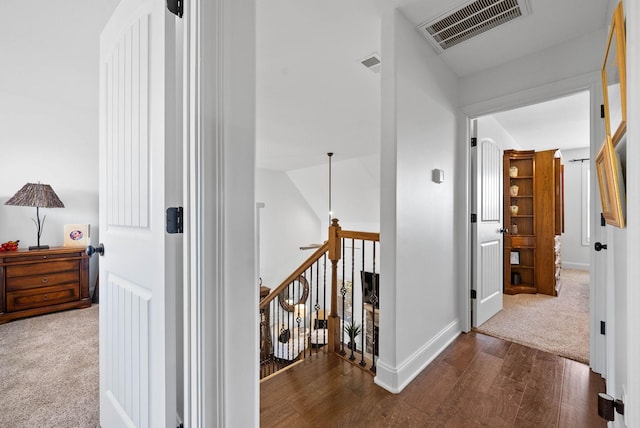 hallway with baseboards, visible vents, an upstairs landing, and wood finished floors