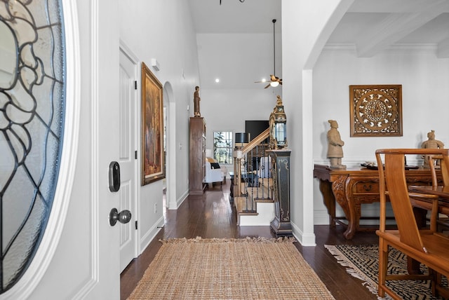 foyer entrance featuring dark wood-style floors, arched walkways, beamed ceiling, and stairway