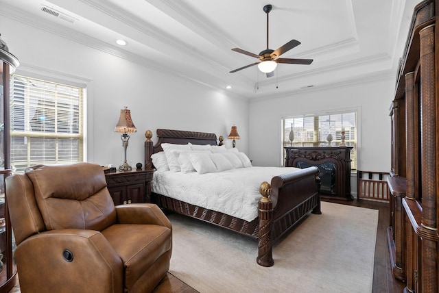 bedroom featuring visible vents, a raised ceiling, a ceiling fan, ornamental molding, and wood finished floors