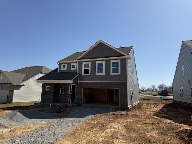 view of front of house with gravel driveway, board and batten siding, an attached garage, and brick siding