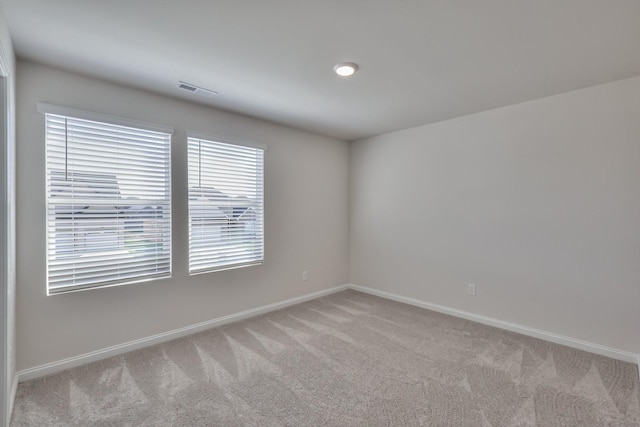 spare room with light colored carpet, visible vents, and baseboards