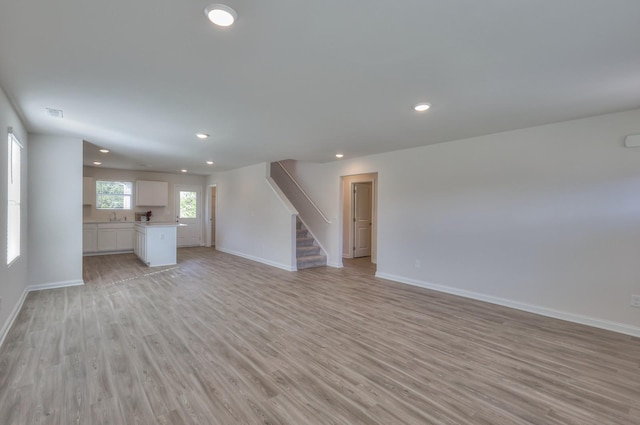 unfurnished living room with recessed lighting, light wood-style flooring, stairway, a sink, and baseboards