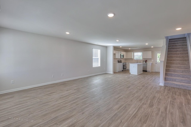 unfurnished living room with light wood-style flooring, plenty of natural light, stairway, and baseboards