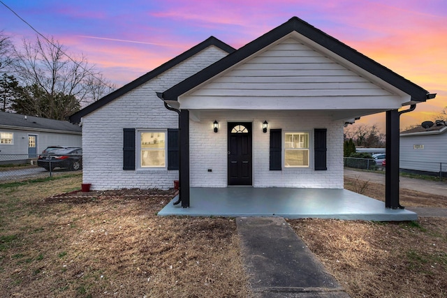 bungalow-style house featuring a porch, brick siding, and fence