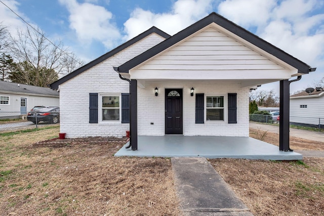 bungalow featuring brick siding, a porch, fence, and a front yard