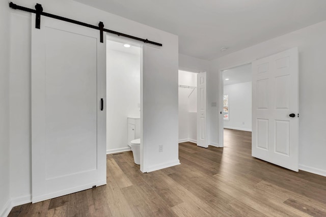 unfurnished bedroom featuring a spacious closet, a barn door, wood finished floors, and baseboards