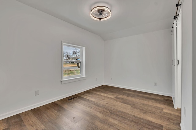 empty room with dark wood-type flooring, visible vents, baseboards, and a barn door