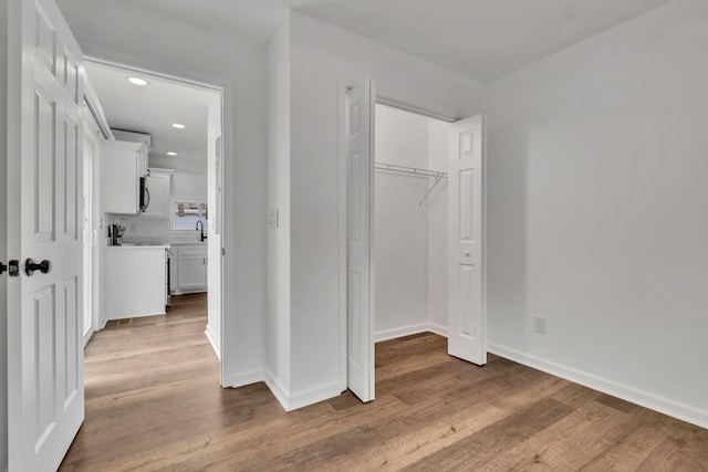 unfurnished bedroom featuring recessed lighting, wood finished floors, a sink, baseboards, and a closet