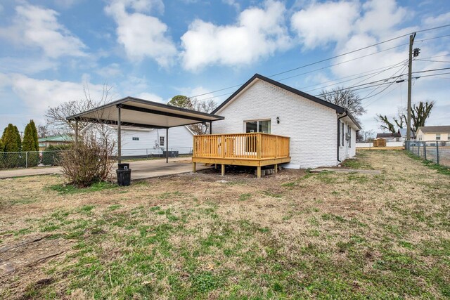 back of property with brick siding, a wooden deck, fence, a yard, and a detached carport