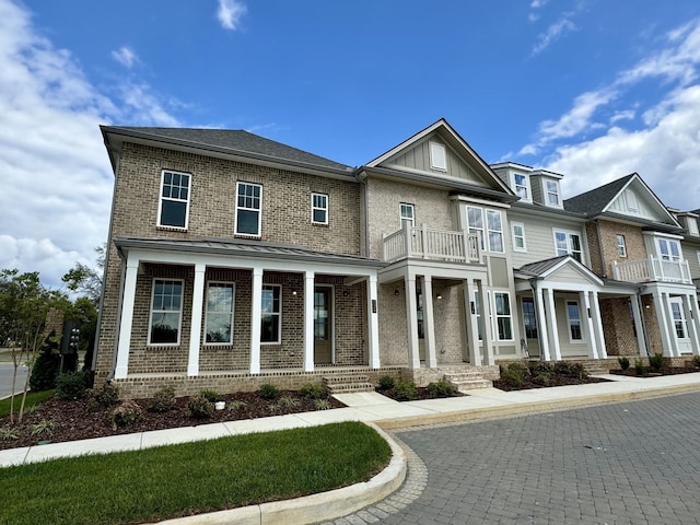 view of front of property with board and batten siding, brick siding, a porch, and a balcony