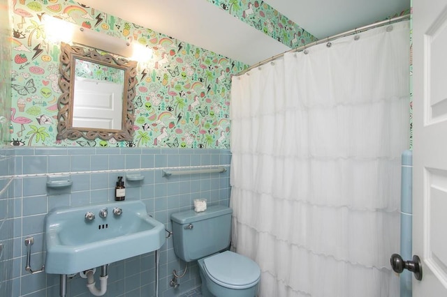 bathroom with wallpapered walls, toilet, a shower with curtain, a wainscoted wall, and a sink