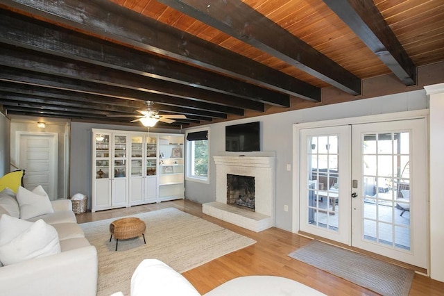 living room featuring a ceiling fan, wood finished floors, french doors, a fireplace, and beam ceiling