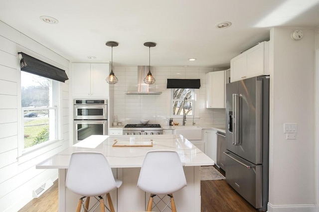 kitchen featuring dark wood-style floors, wall chimney exhaust hood, appliances with stainless steel finishes, and tasteful backsplash