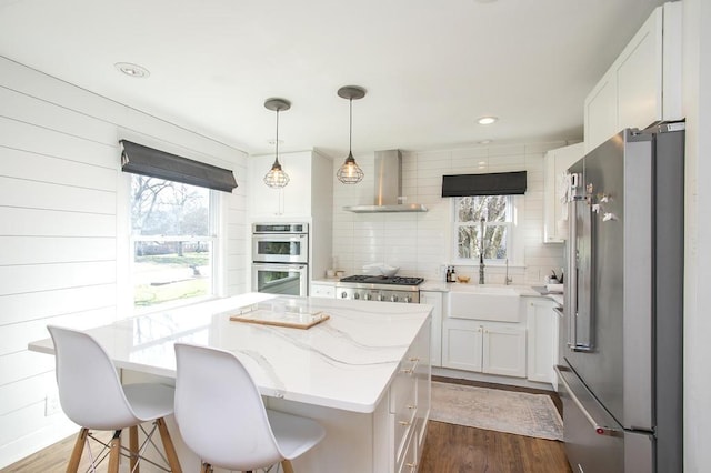 kitchen with plenty of natural light, wall chimney exhaust hood, a kitchen island, and appliances with stainless steel finishes