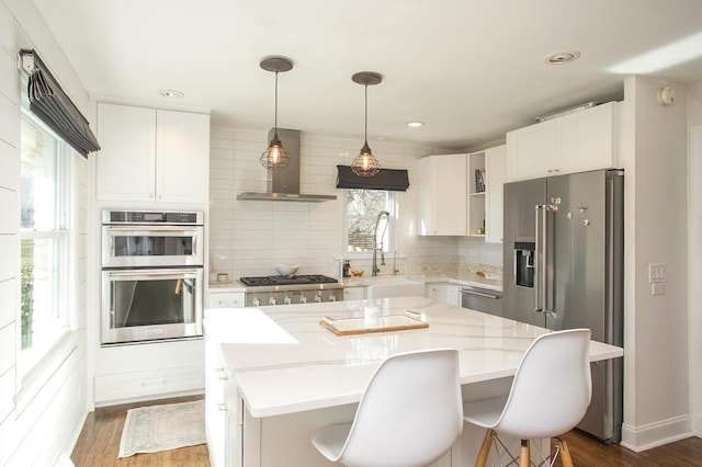 kitchen featuring wall chimney exhaust hood, appliances with stainless steel finishes, a sink, and decorative backsplash