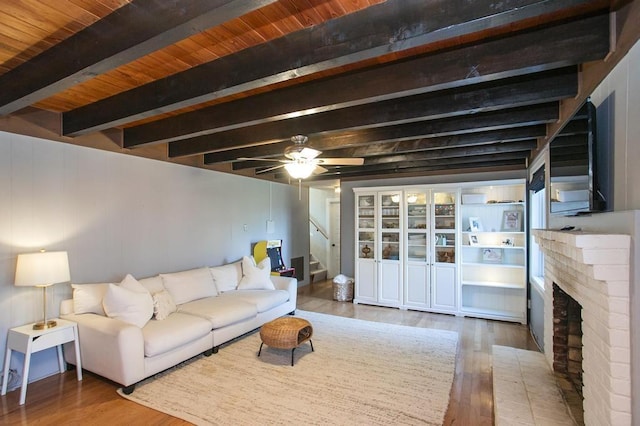 living area with stairway, a brick fireplace, ceiling fan, wood finished floors, and beamed ceiling