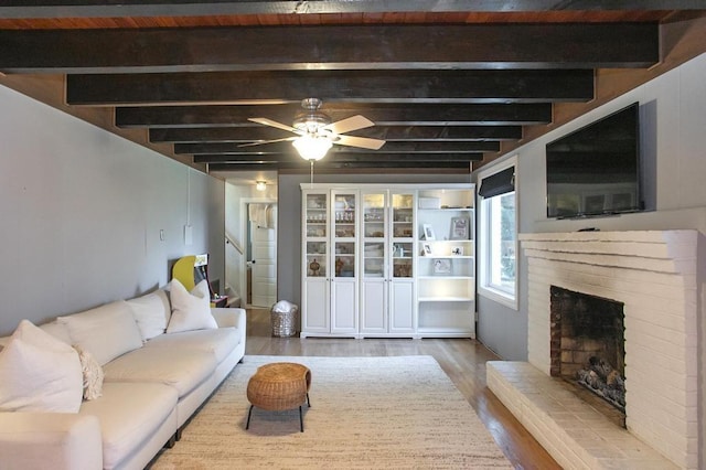 living room with ceiling fan, beamed ceiling, a fireplace, and wood finished floors