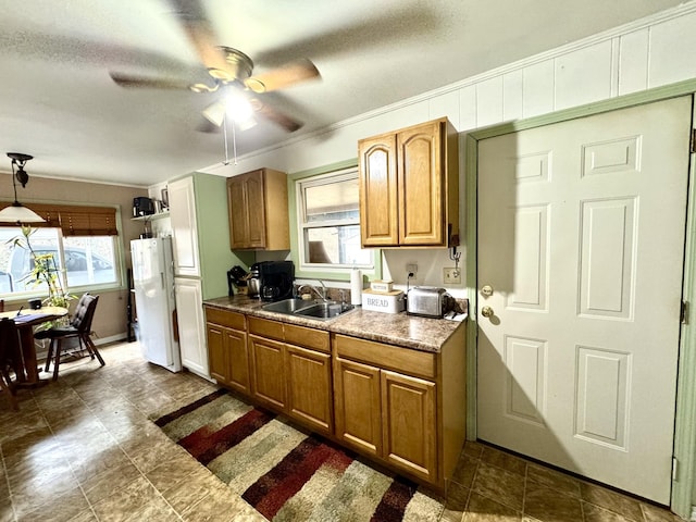 kitchen featuring decorative light fixtures, brown cabinetry, freestanding refrigerator, a sink, and ceiling fan