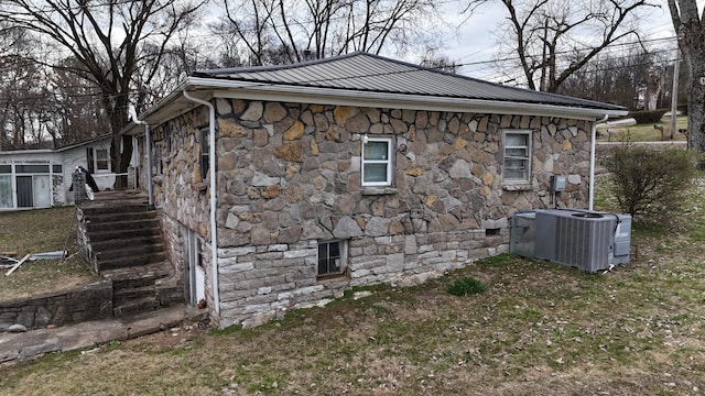 view of side of property with central air condition unit, crawl space, stone siding, and metal roof