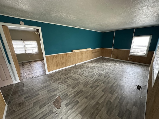 spare room with visible vents, a wainscoted wall, a textured ceiling, and wood finished floors